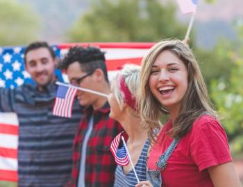 friends smiling as they hold American flags for a fourth of july event