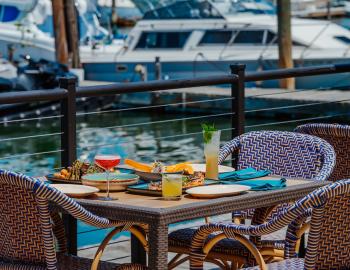 A table for two on a restaurant's waterfront patio with a harbor and boats in the background