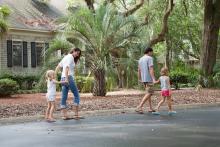 Mother and father walking down street with two small children in a coastal beach neighborhood.