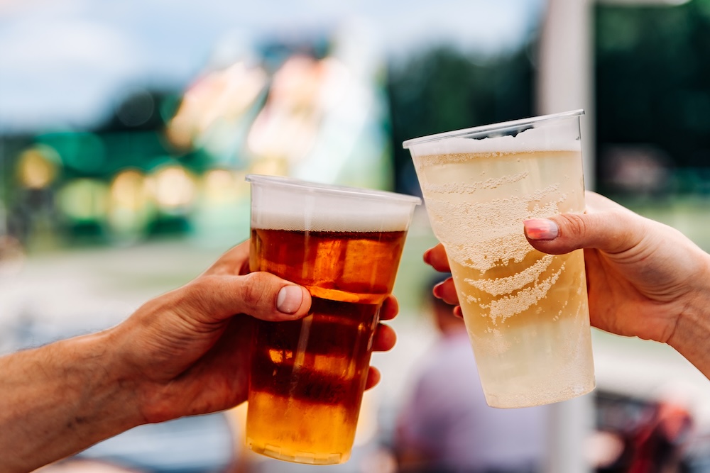 Two people clinking beer glasses together at an outdoor event