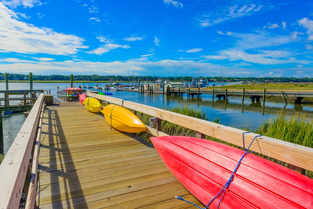 Kayaks resting against the dock railing with a marsh and harbor in the background